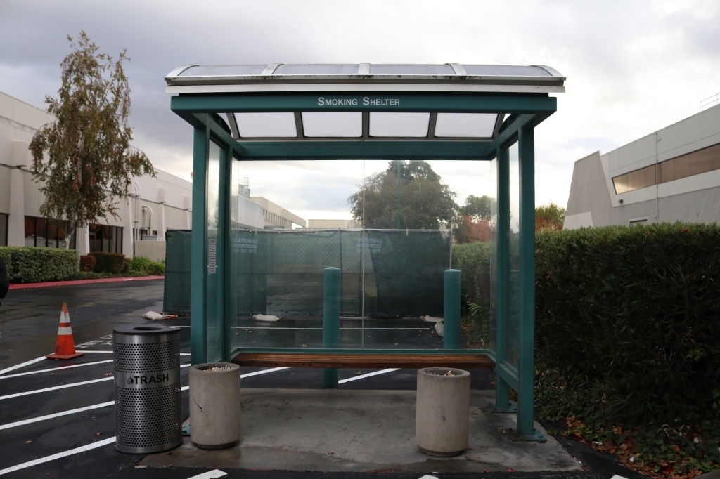 Another image of the smoking shelter. This one is slightly cleaner, the trash can isnt overflowing, and there are two ash trays instead of one.  